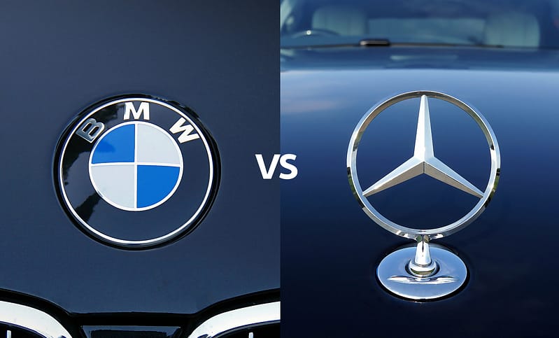 Two oposing photos of BMW and Mercedes-Benz hood ornaments, with the text "VS" between them